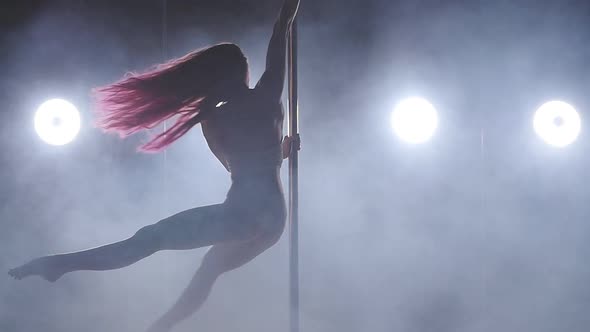 Young Woman on a Pole Dancing in a Dark Room with Backlight and Smoke