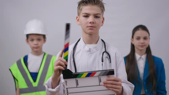 Smiling Boy in Medical Gown Posing with Clapper Board As Friends Builder and Photographer Crossing