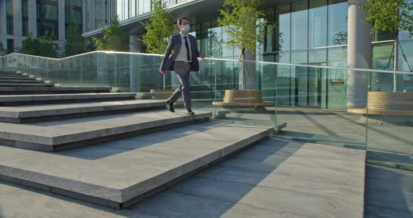 Businessman in a Protective Mask Descends the Stairs of the Business Center and for the Joy of a