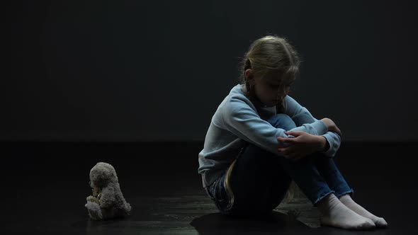 Depressed Little Girl Feeling Lonely, Hugging Teddy Bear, Sitting in Dark Room