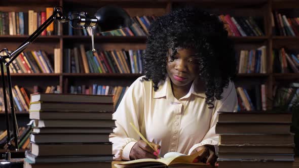 AfricanAmerican Lady Writes Near Stacks of Books at Table