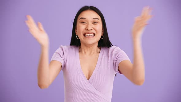 Surprised Asian brunette woman wearing purple t-shirt clapping hands at the camera
