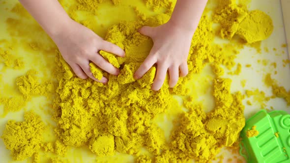 Close up of kids hands playing with yellow magic sand, top view