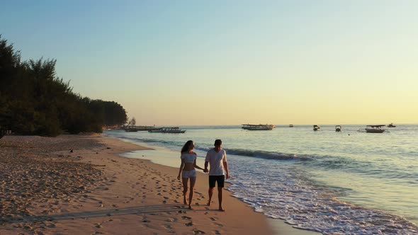 Hand-held couple in love enjoying first rays of sunny day, walking on exotic beach washed by sea wav