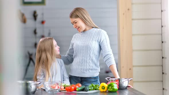 A Young Pretty Mother and Her Cute Daughter are Cooking Salad Together