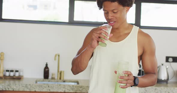 Fit african american man cooking, drinking healthy green smoothie