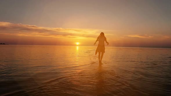 Brunette Woman in a Dress Running Along Water at Sunset or Sunrise