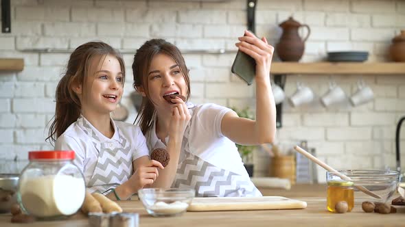 Two sisters (or mother daughter) having fun and taking selfies at the kitchen.