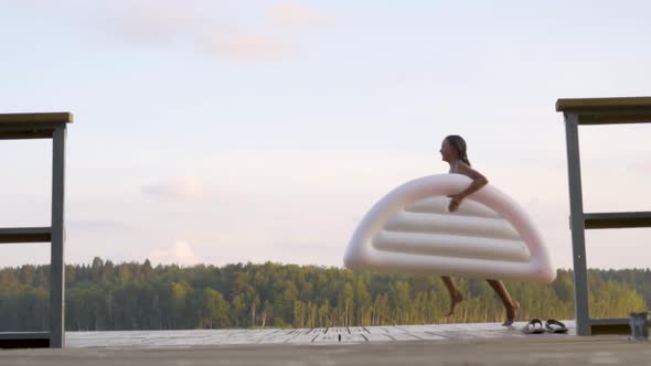 Teenager Runs with Air Mattress at the Lake on Wooden Pier