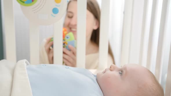 Portrait of Young Mother Looking Through Wooden Cradle Banister on Her Little Baby Lying in Cradle