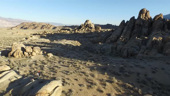 Aerial shot of a young man backpacking with his dog in a mountainous desert.