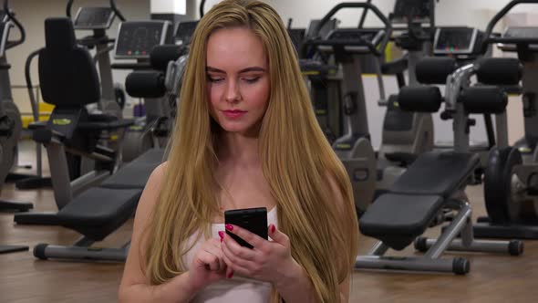 A Young Beautiful Woman Works on a Smartphone in a Gym - Closeup