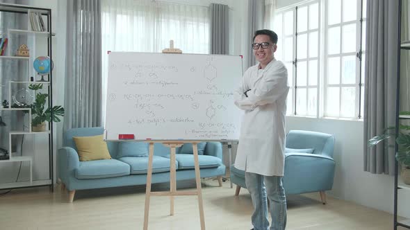 Asian Male Teacher With Glasses Crossing Arms And Smiling To Camera While Teaching Chemist At Home