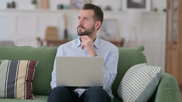 Pensive Young Man with Laptop Thinking on Sofa