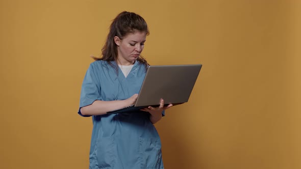Portrait of Busy Medic Standing Holding Laptop Looking Confused at Screen and Typing on Keyboard