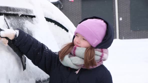 Child a Little Cute Girl Cleans the Car From Snow on a Snowy Winter Day