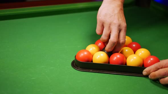 A man setting up the pool balls on a table in a triangle. He spins the eight ball