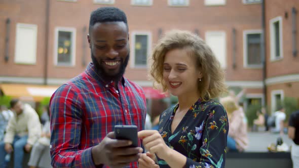 Happy Diverse Young Couple Surfing Internet on Mobile Phone Outdoors