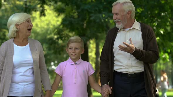 Little Boy Walking With His Grandparents in Park, Enjoying Happy Time Together