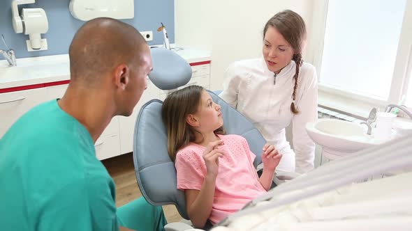 Little girl sitting in the dental chair, talking with dentist and assistant