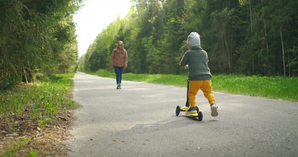 Mother and Son Drive Scooter Outdoors. He's Always Making Us so Proud. Cute Little Boy Wearing Cap