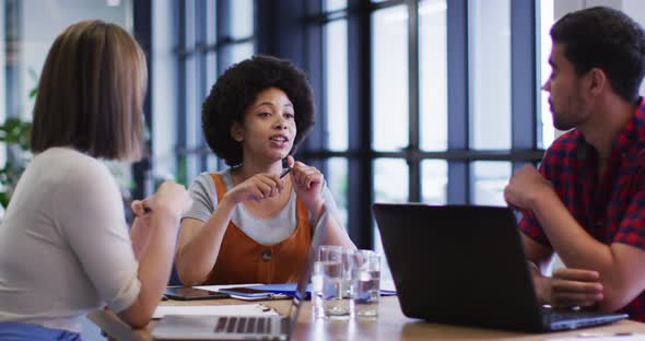 Diverse business people sitting using laptop going through paperwork in modern office