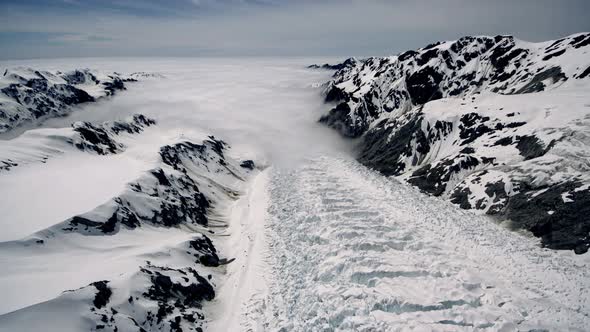 High alpine polar glacier draining in stony rugged moutain tops. fog mist over wide snow surface on