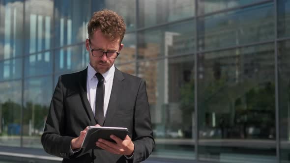 Businessman Working on Tablet Standing Next To Office Building