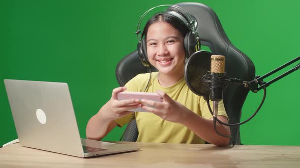 Excited Asian Kid Girl Playing Video Game With Phone Then Smiles To Camera On Green Screen alt