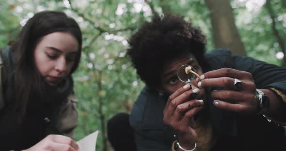 Man examines with microscope while Woman makes notes