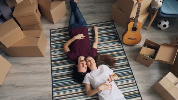 Top View of Happy Man and Woman Talking Lying on Carpet in New Flat with Boxes