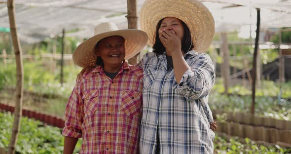 Happy Asian woman farmers looking to camera and laughing together on local organic vegetable farm.