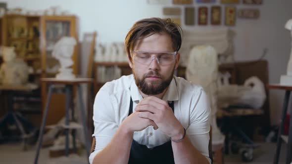 Young Modern Bearded Master in Special Glasses Looking at Camera in His Studio