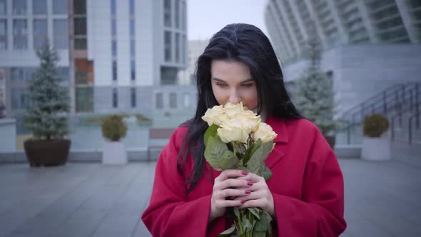 Portrait of Romantic Young Caucasian Woman Smelling Yellow Roses and Looking at Camera, Fashionable