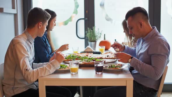 Four Young Friends Are Talking During a Meal with Big Pizza in a Restaurant