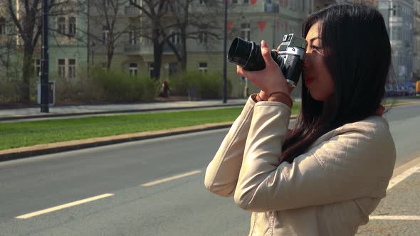 A Young Asian Woman Takes Pictures with a Camera in a Street in an Urban Area