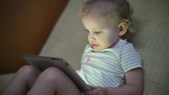 child looking at a tablet sitting on a sofa. Little girl and internet