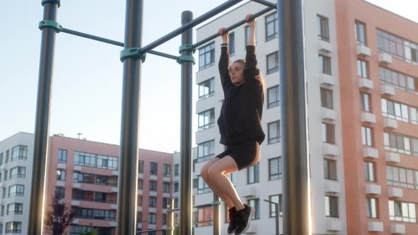 Young Woman Warms Up on Horizontal Bar in Morning in Residential Complex