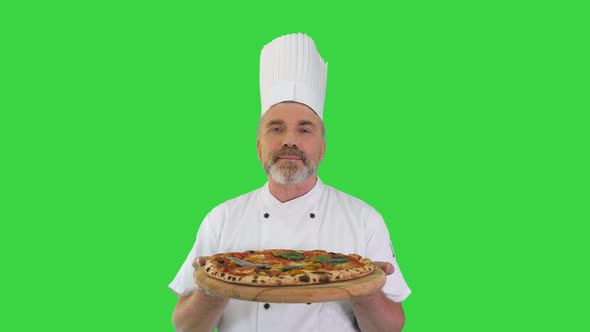 Happy Senior Cook with a Pizza in Hands Looking To Camera on a Green Screen Chroma Key