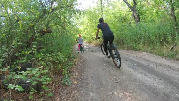 Mom and Daughter Ride Bicycles in the Forest in Summer