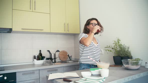 A Young Cheerful Woman Drinks Wine From a Glass While Enjoying Cooking