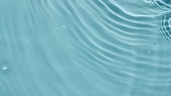 Top View Slow Motion of Drop Falls Into Water and Diverging Circles of Water on Blue Background