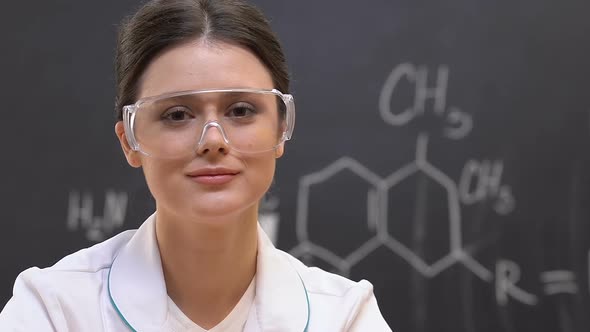 Young Female Scientist Looking at Camera, Chemical Formula on Background