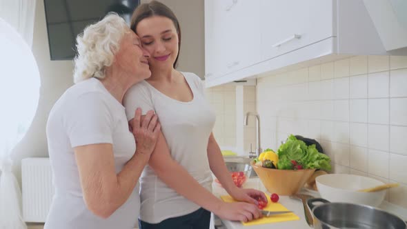 Old Woman Hugging Granddaughter in Kitchen