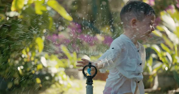 Cute Happy Child Playing with Garden Sprinkler on Summer Hot Day