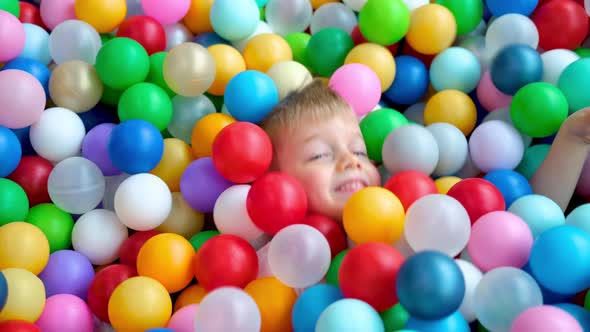 Blonde Little Boy Lying on Multi Coloured Plastic Balls in Big Dry Paddling Pool in Playing Centre