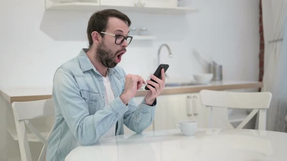 Beard Young Man Celebrating Success on Smartphone in Office 