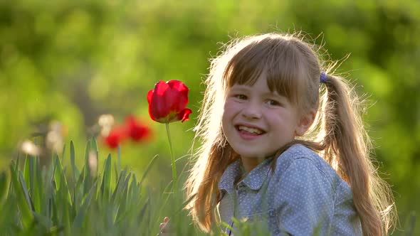 Pretty Child Girl Smiling Happily Near Red Flower in Summer