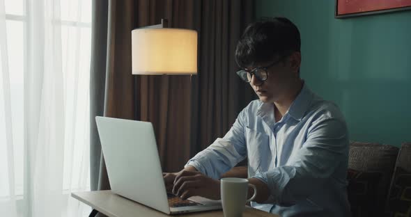 Young Attractive Asian Vietnam Man Busy Work Computer or Smart Tablet on Laptop at Home in Freelance