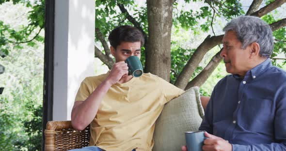 Young biracial man drinking coffee while listening to father's conversation at patio